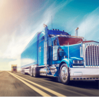 Large blue truck driving fast on the road with a truck behind blurred in the distance. The trucking industry depends on high-quality springs for optimal safety and efficiency.